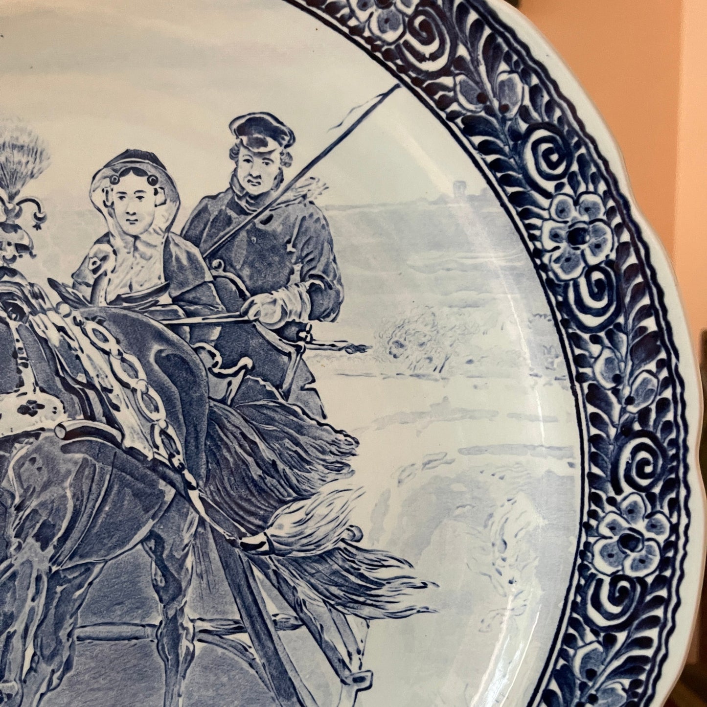 Decorative plate with blue and white design of a person on horseback and another person, possibly a woman, holding a child.