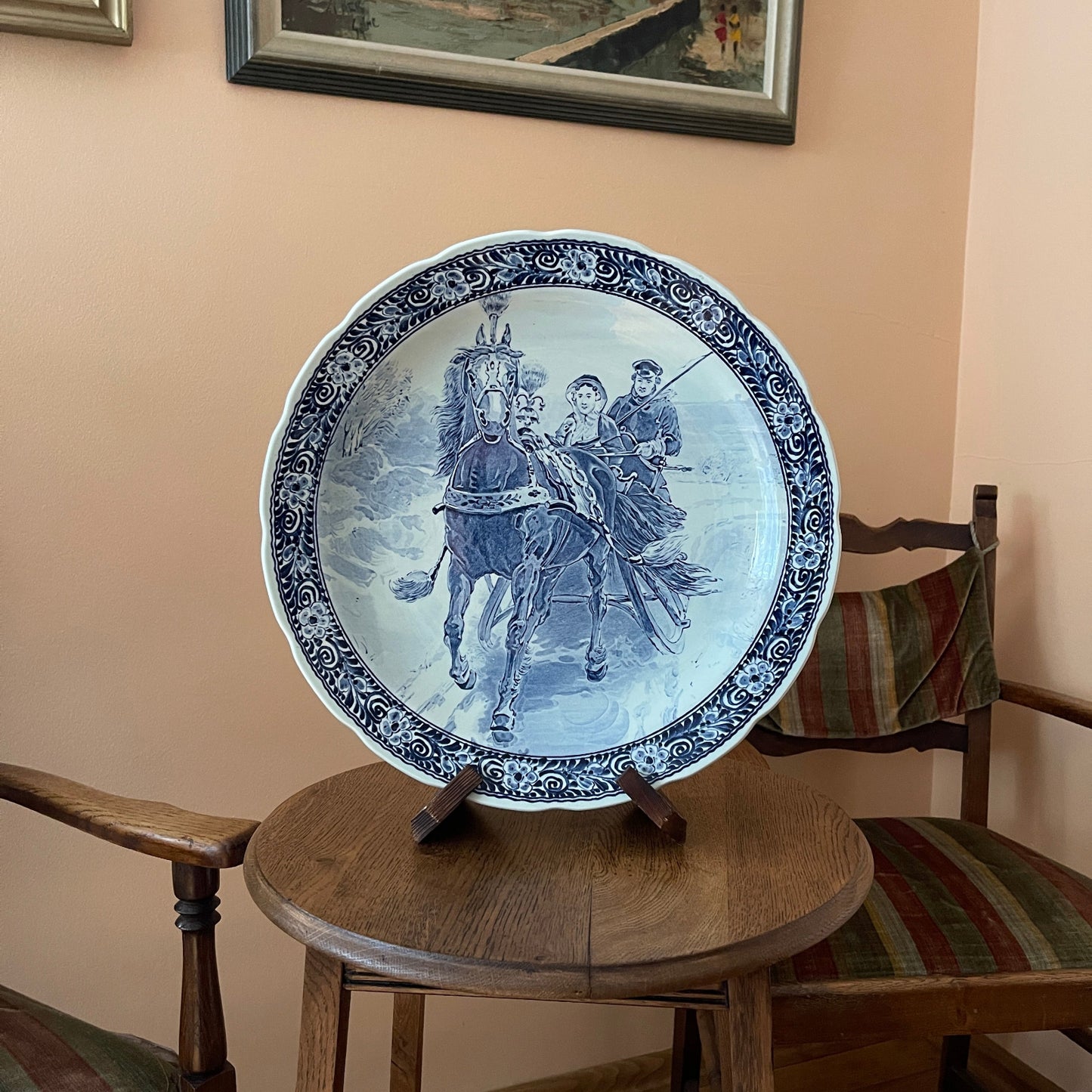 Decorative plate with historical design on a wooden stool against a beige wall.