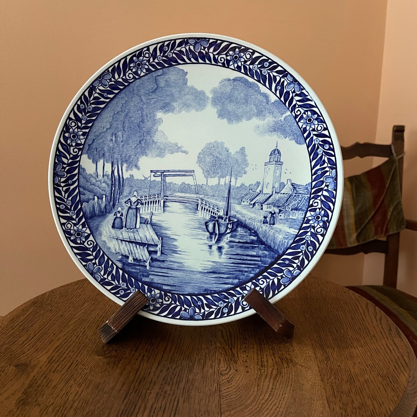 Decorative plate with blue and white design on a wooden stand against a beige wall.
