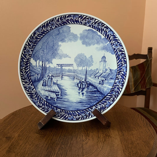 Decorative plate with blue and white design on a wooden stand against a beige wall.