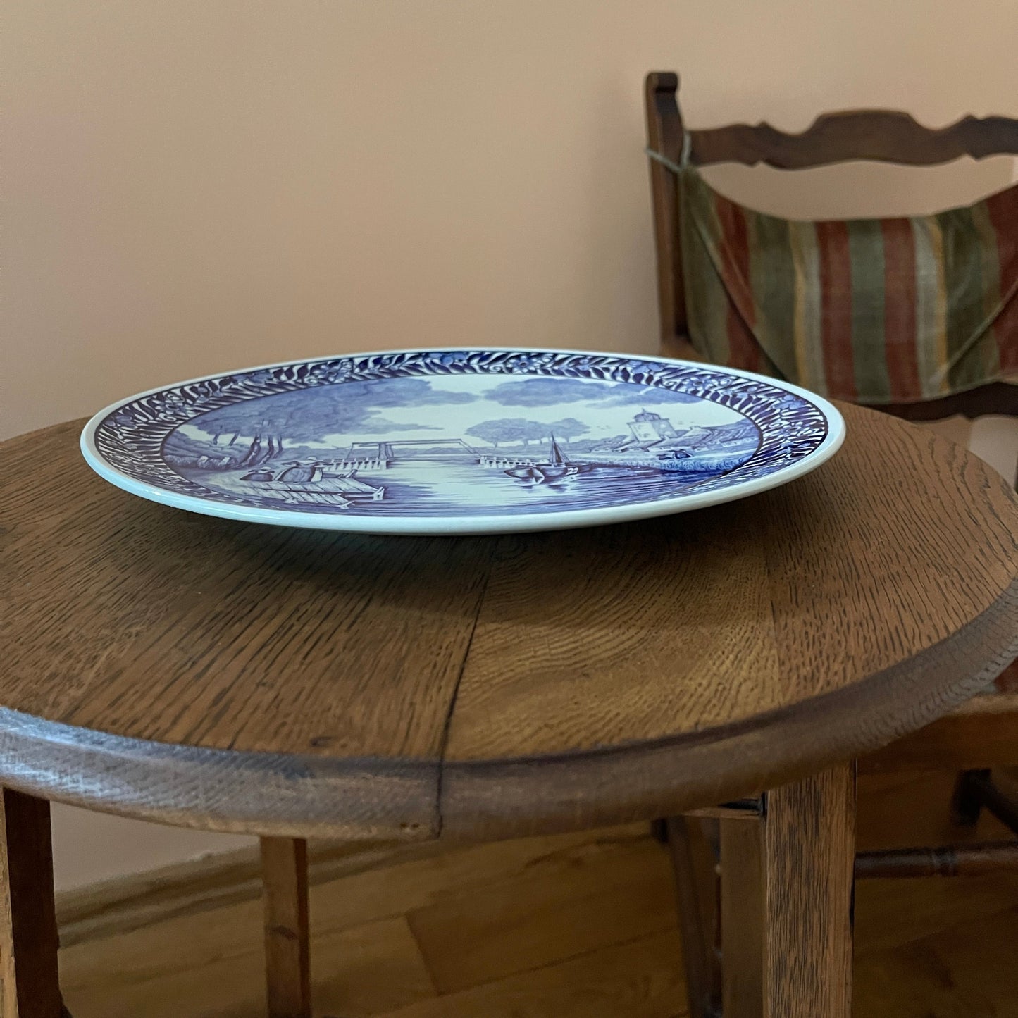 Blue and white decorative plate on a wooden table with a chair in the background