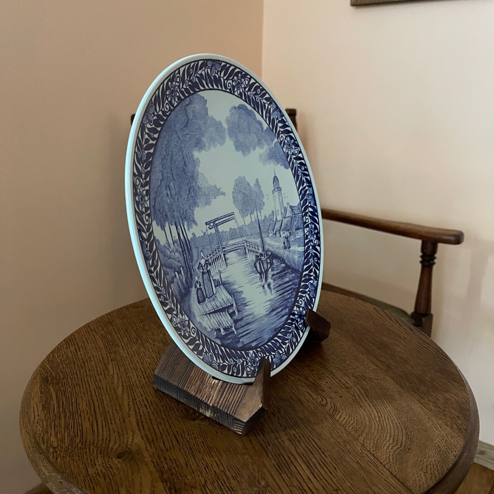 Decorative blue and white plate on a wooden stand against a beige wall.