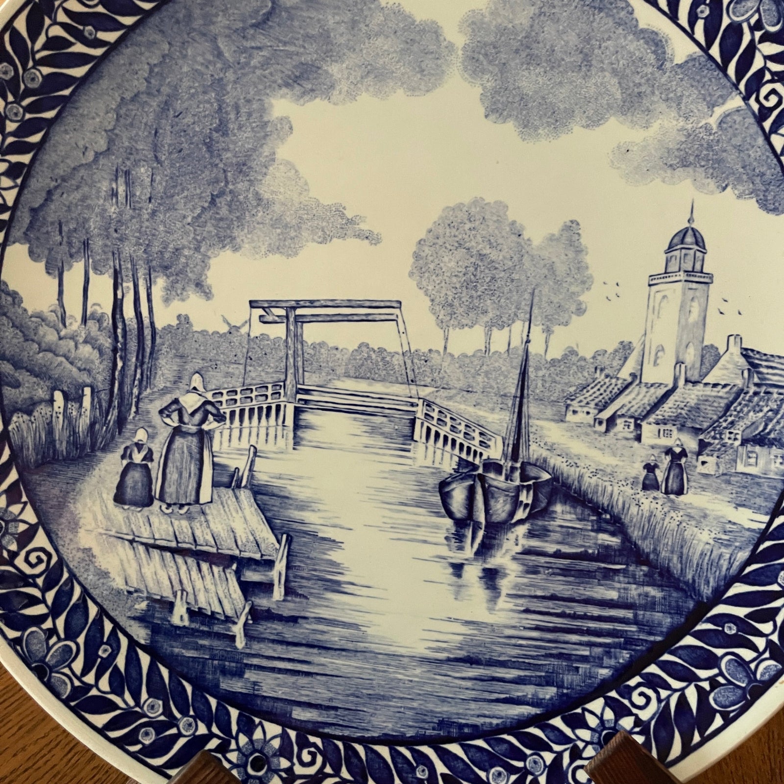 Decorative plate with a blue and white scene of a village by a river with a bridge and boat.