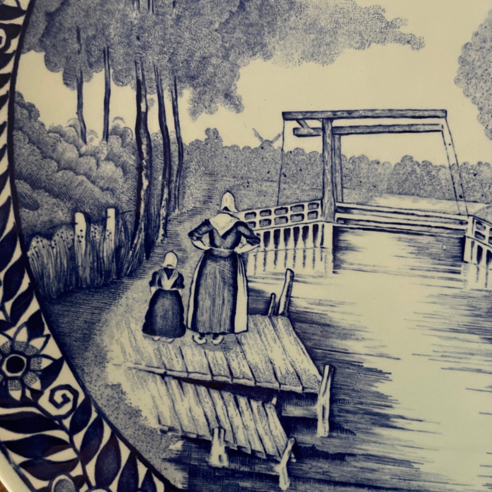 Black and white illustration of two people on a dock by a lake with trees in the background.