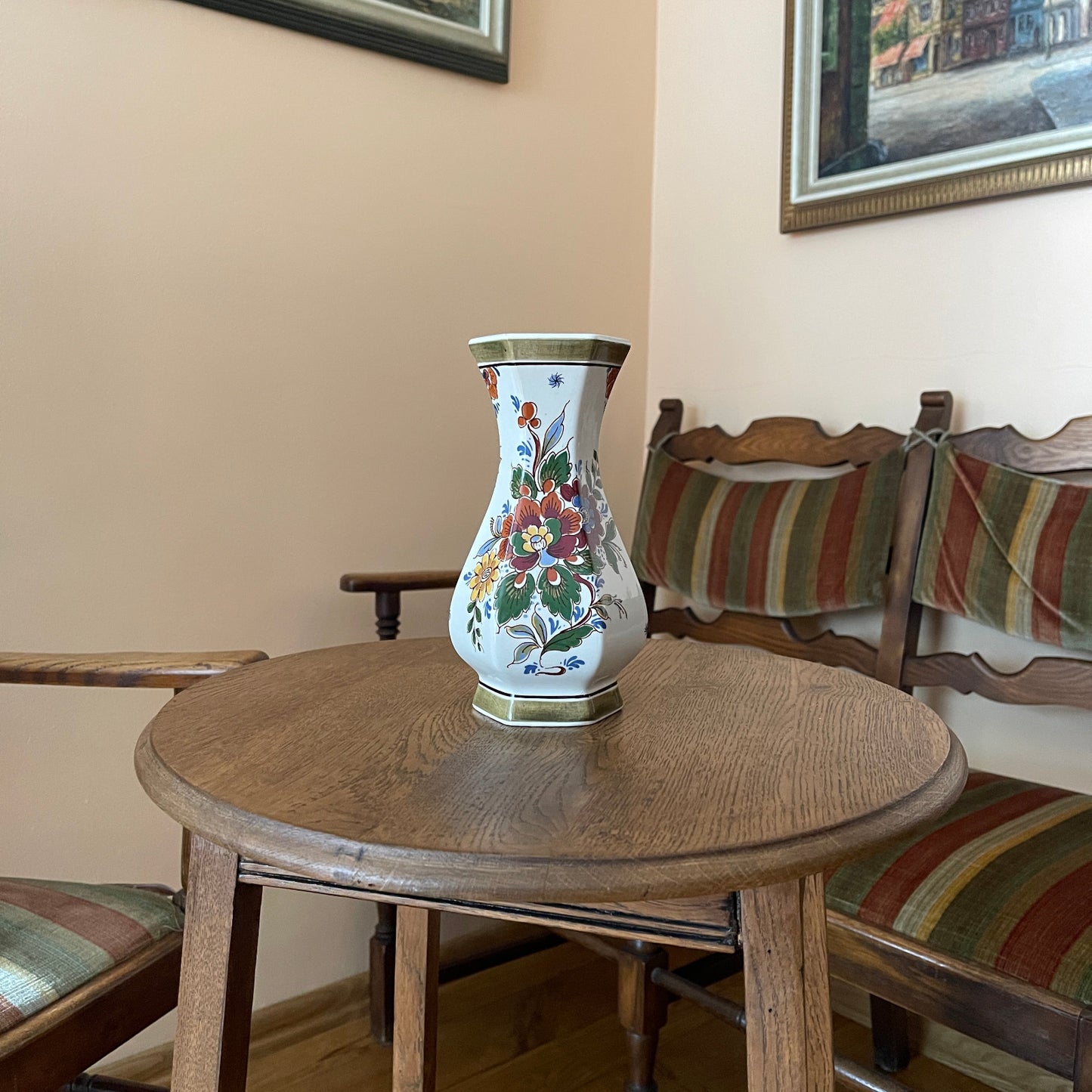 Decorative vase on a wooden table with striped chairs and framed pictures in the background