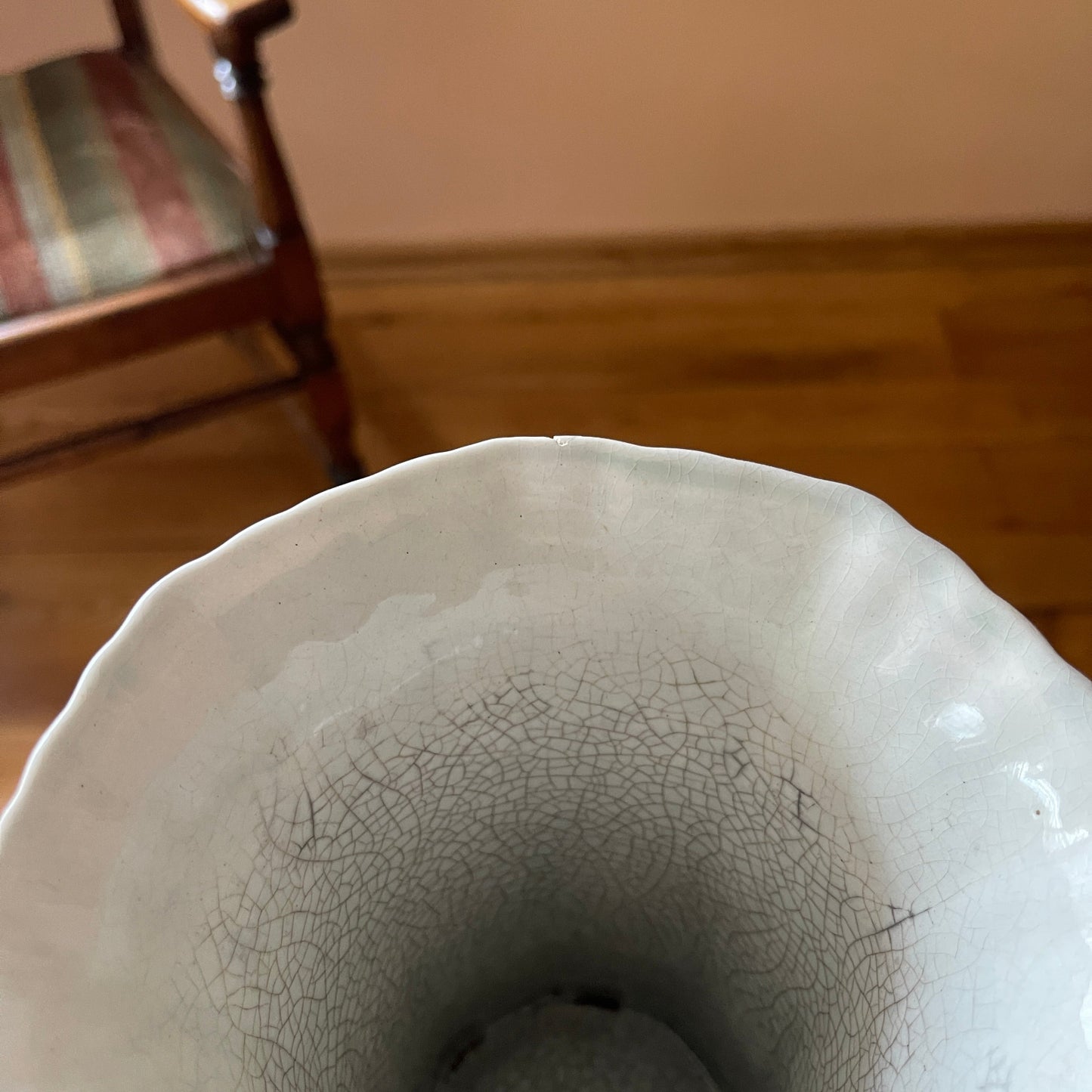 Close-up of a cracked ceramic vase on a wooden floor.