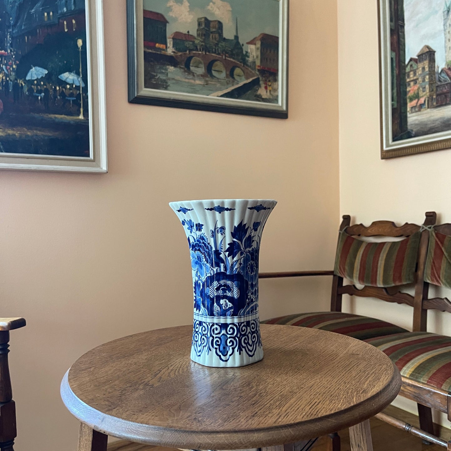 Blue and white floral-patterned vase on a wooden table with framed pictures on the wall.