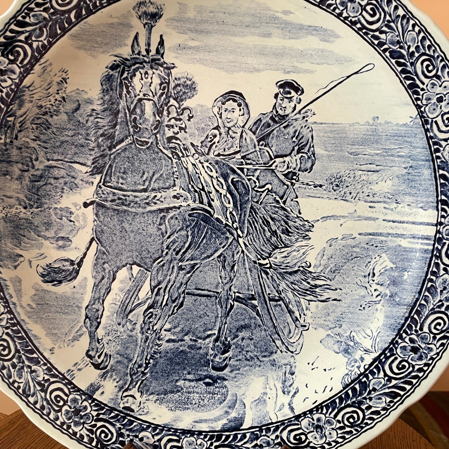 Decorative plate with a black and white illustration of a horse and two people riding it, set against a scenic background.