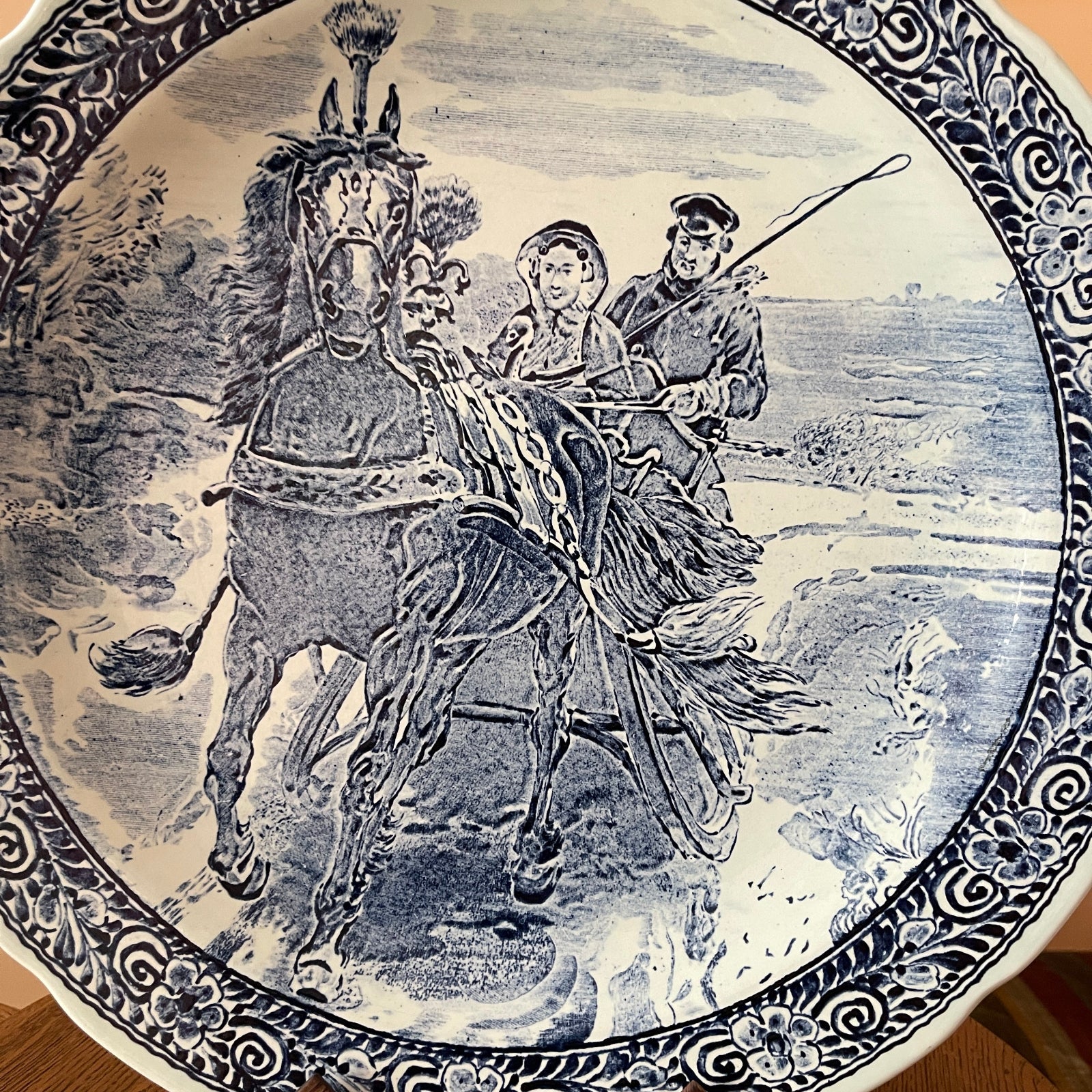 Decorative plate with a black and white illustration of a horse and two people riding it, set against a scenic background.