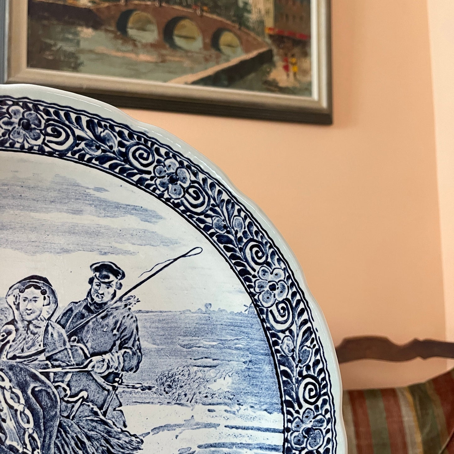 Decorative plate with a scenic design of a couple by a river, framed painting in the background.