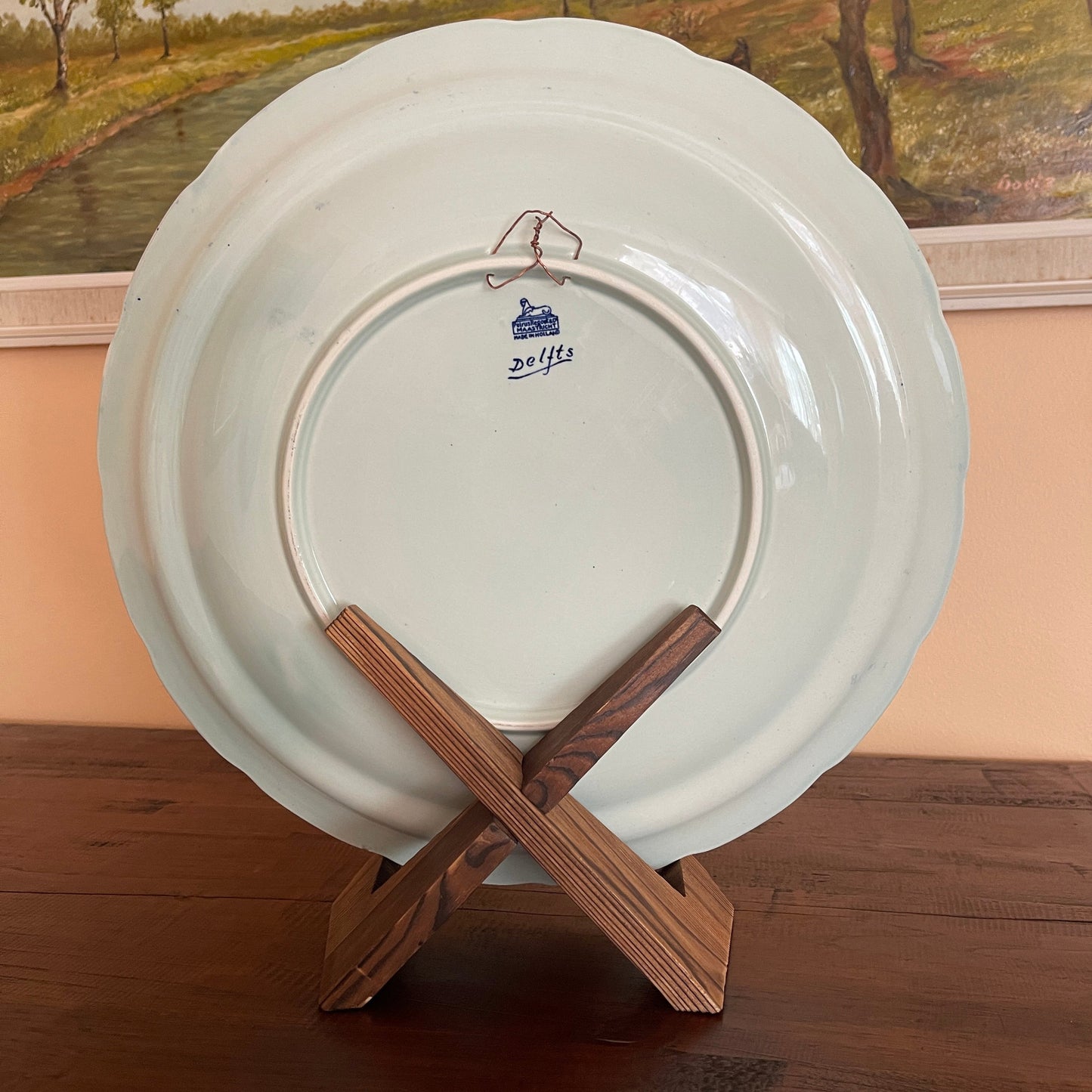White plate with a Dolffs logo on a wooden stand against a painting of a landscape.