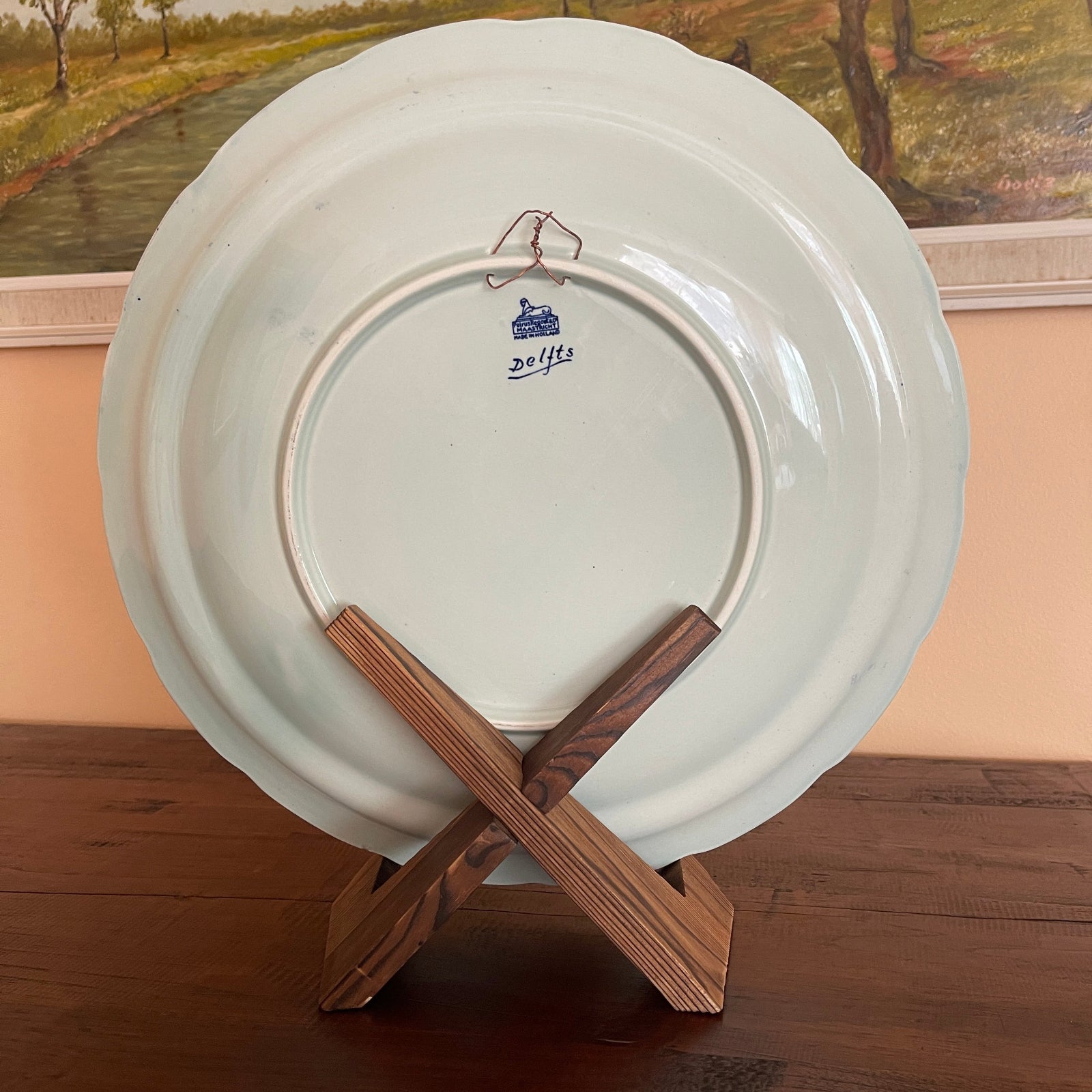 White plate with a Dolffs logo on a wooden stand against a painting of a landscape.