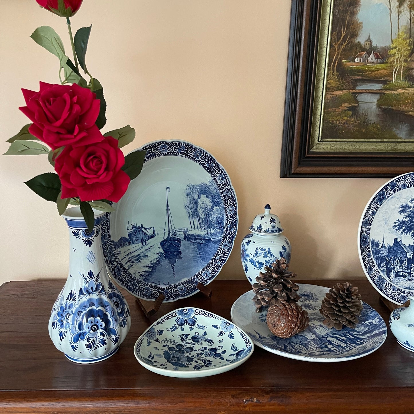 Collection of blue and white ceramic plates and a vase on a wooden surface with a painting in the background.