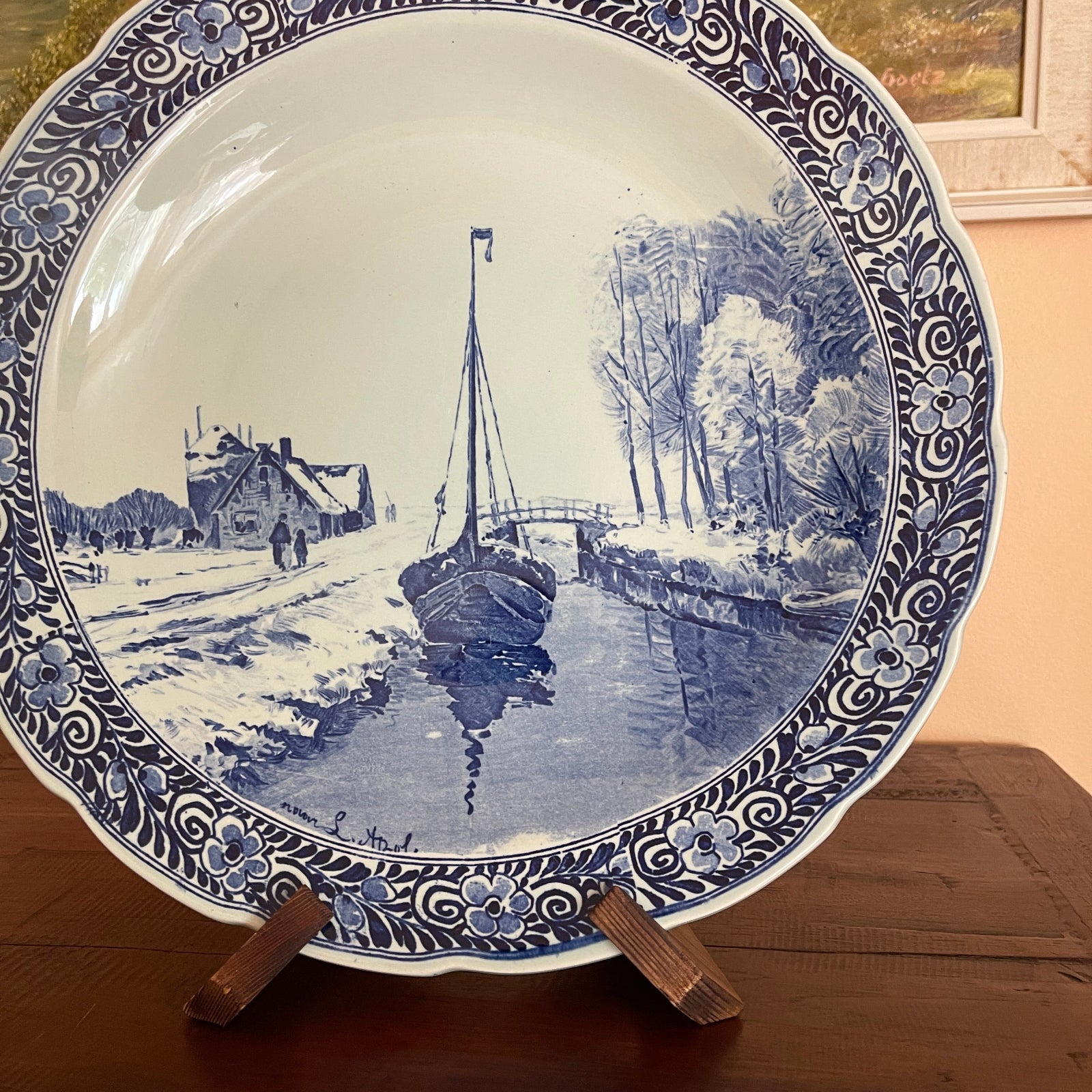Decorative plate with blue and white design of a canal scene on a wooden stand.