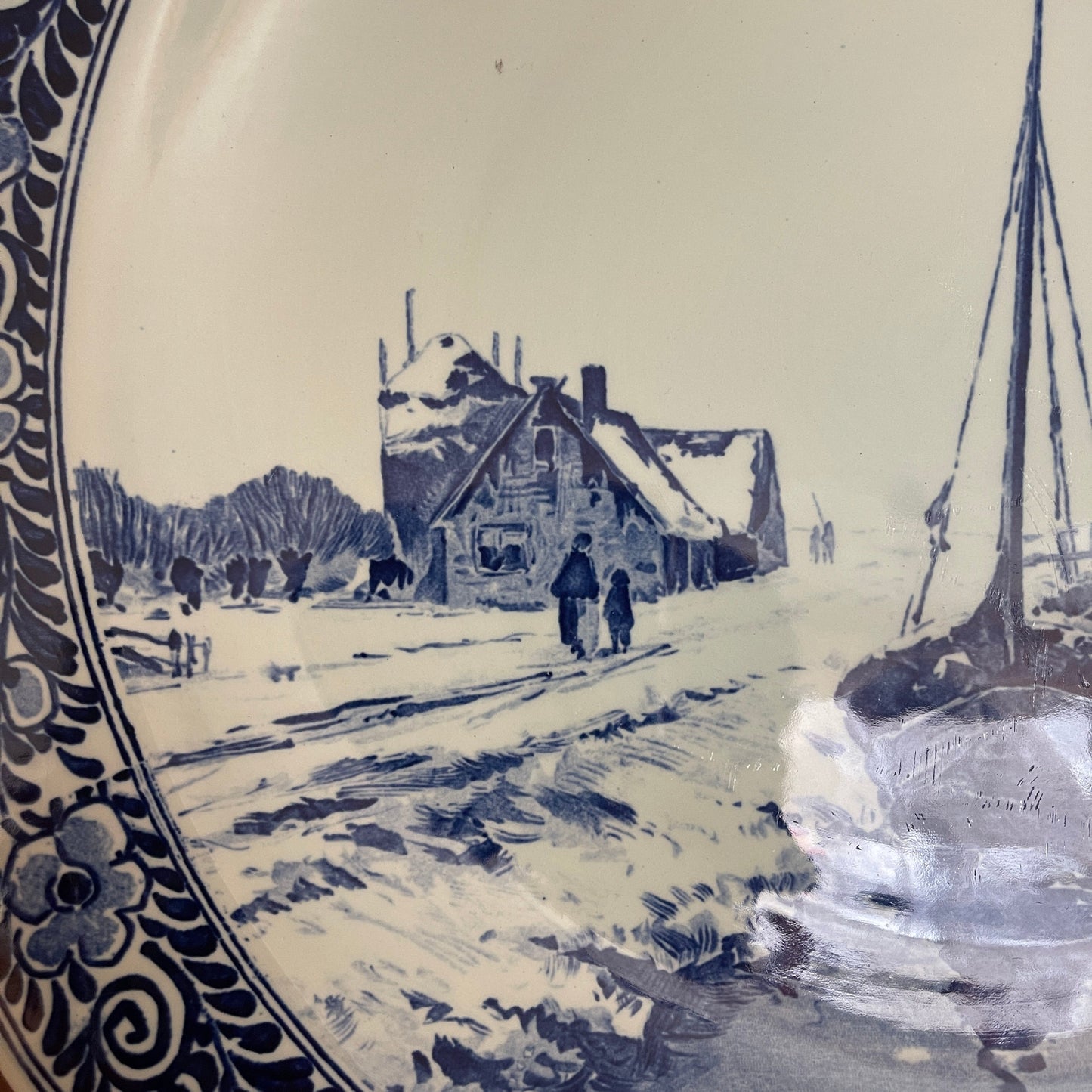 Decorative plate with a winter scene of a house and sailboat, featuring blue and white colors.