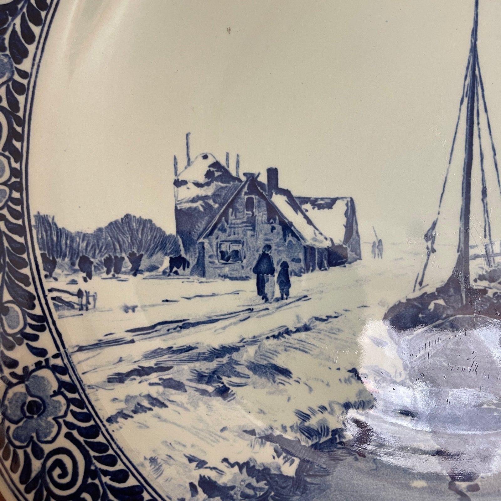 Decorative plate with a winter scene of a house and sailboat, featuring blue and white colors.