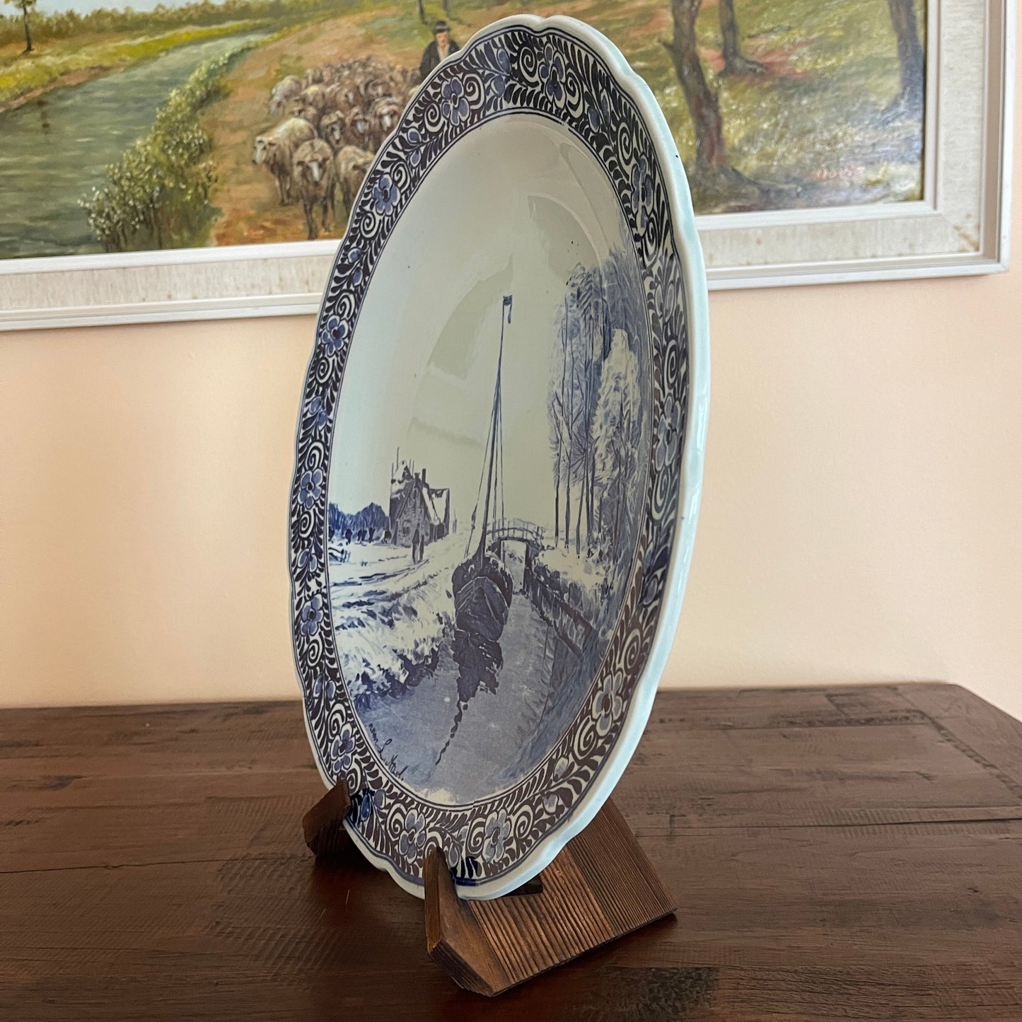 Decorative plate with a blue and white design on a wooden stand, framed artwork in the background.