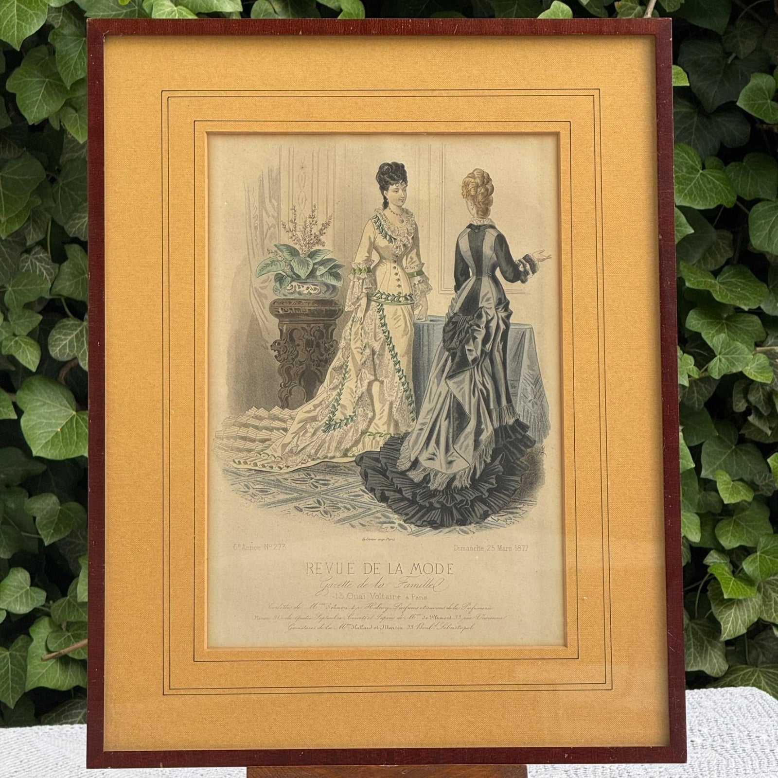 Framed vintage print of two women in elaborate dresses with a decorative border.