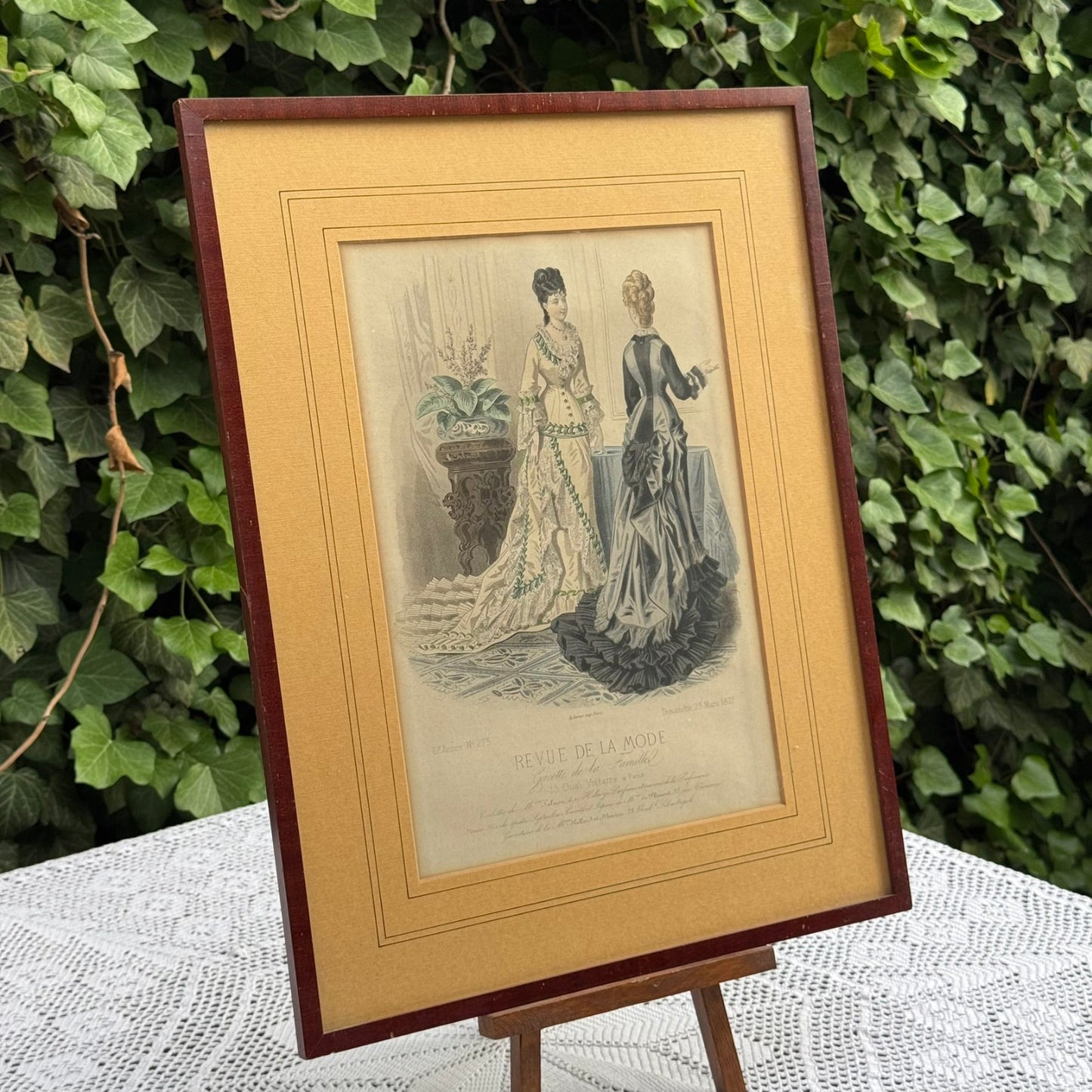 Framed vintage print of two women on an easel with a green leafy background