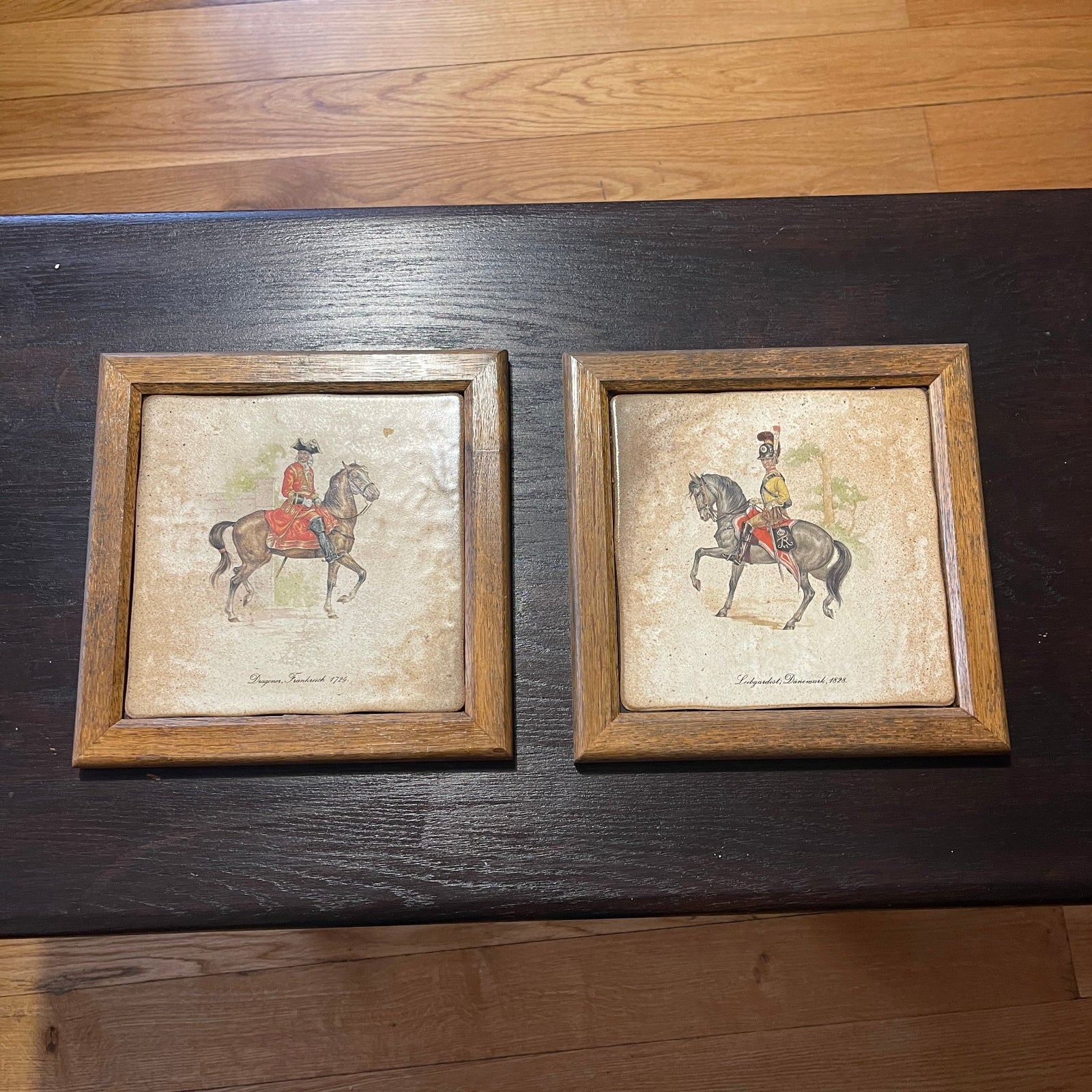 Two framed pictures of a person on horseback on a wooden surface.