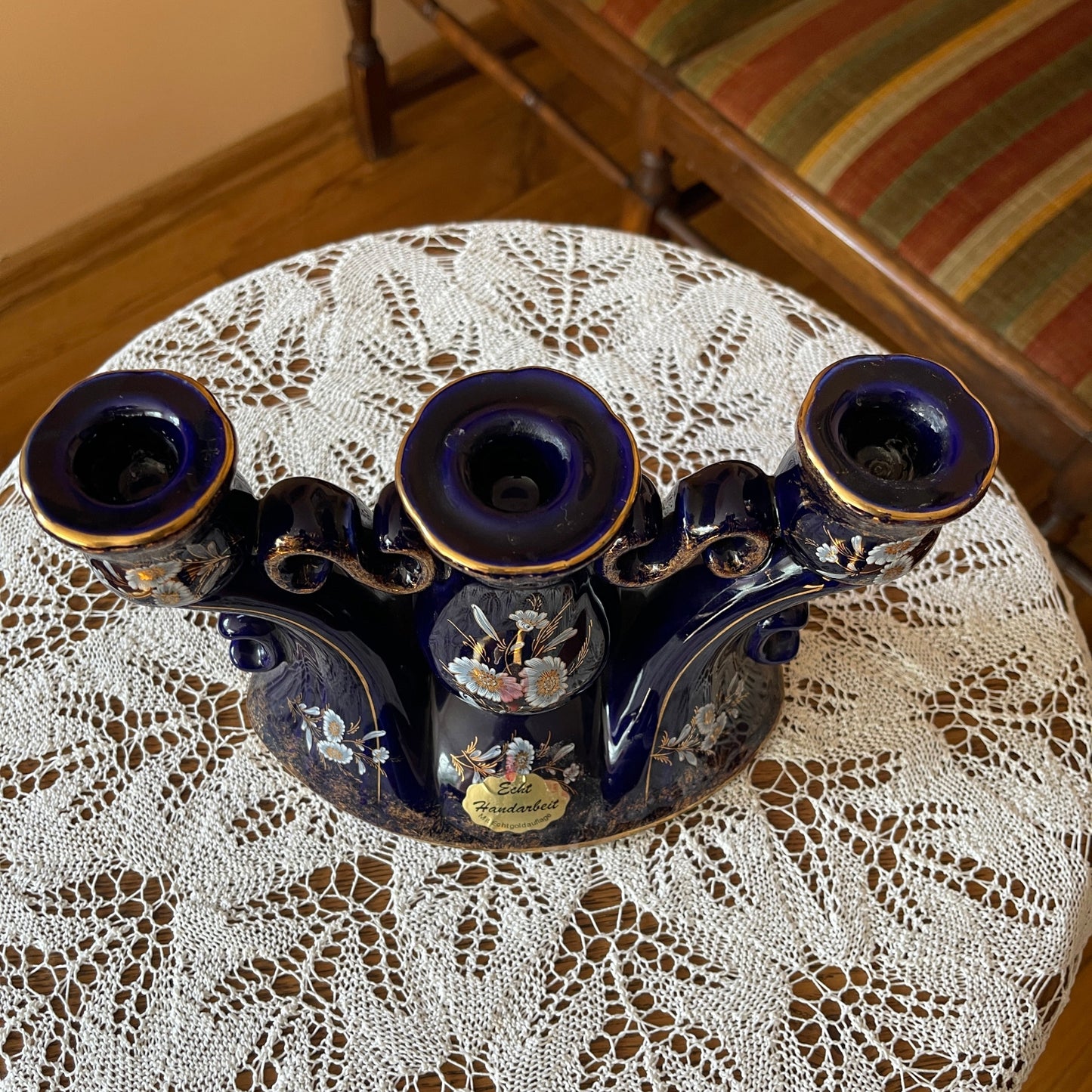 Decorative blue candle holder on a lace tablecloth with a striped chair in the background.