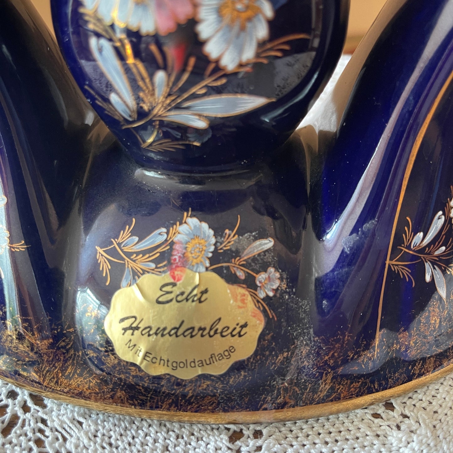 Decorative blue vase with floral design and 'Echt Handarbeit' label on a lace tablecloth.