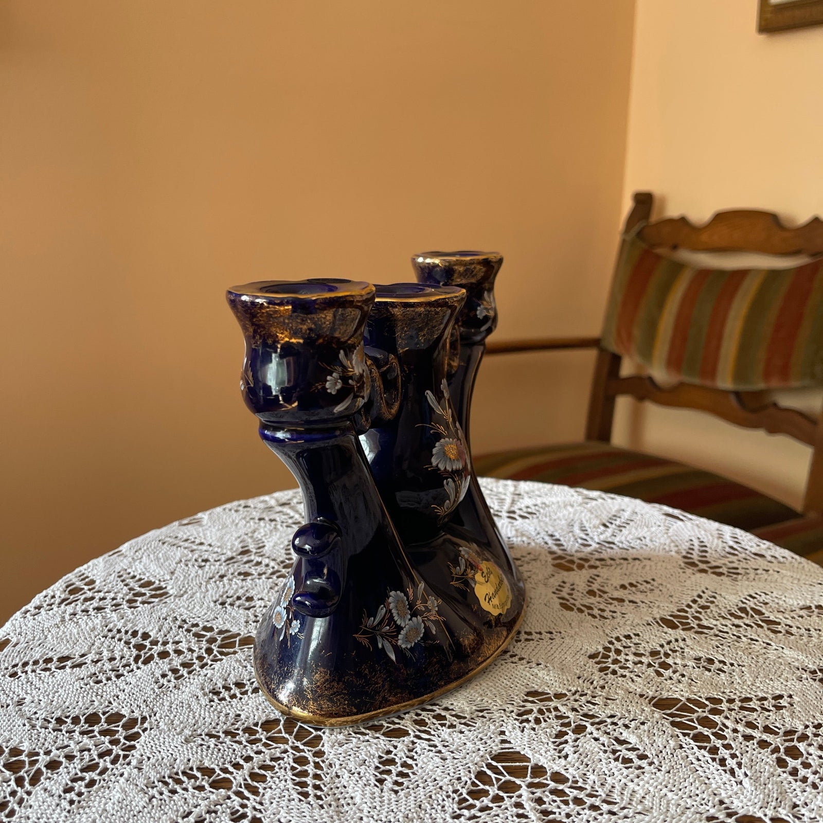 Decorative black vase on a lace tablecloth with a chair in the background