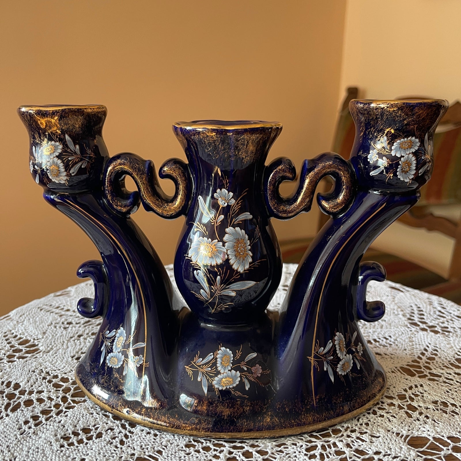 Decorative blue candle holder with floral designs on a lace tablecloth.