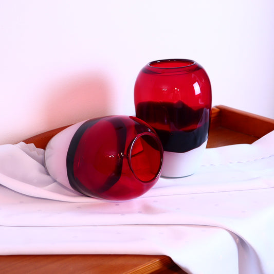 A pair of red, black, and white Murano glass vases of different sizes placed on a surface with a white cloth.