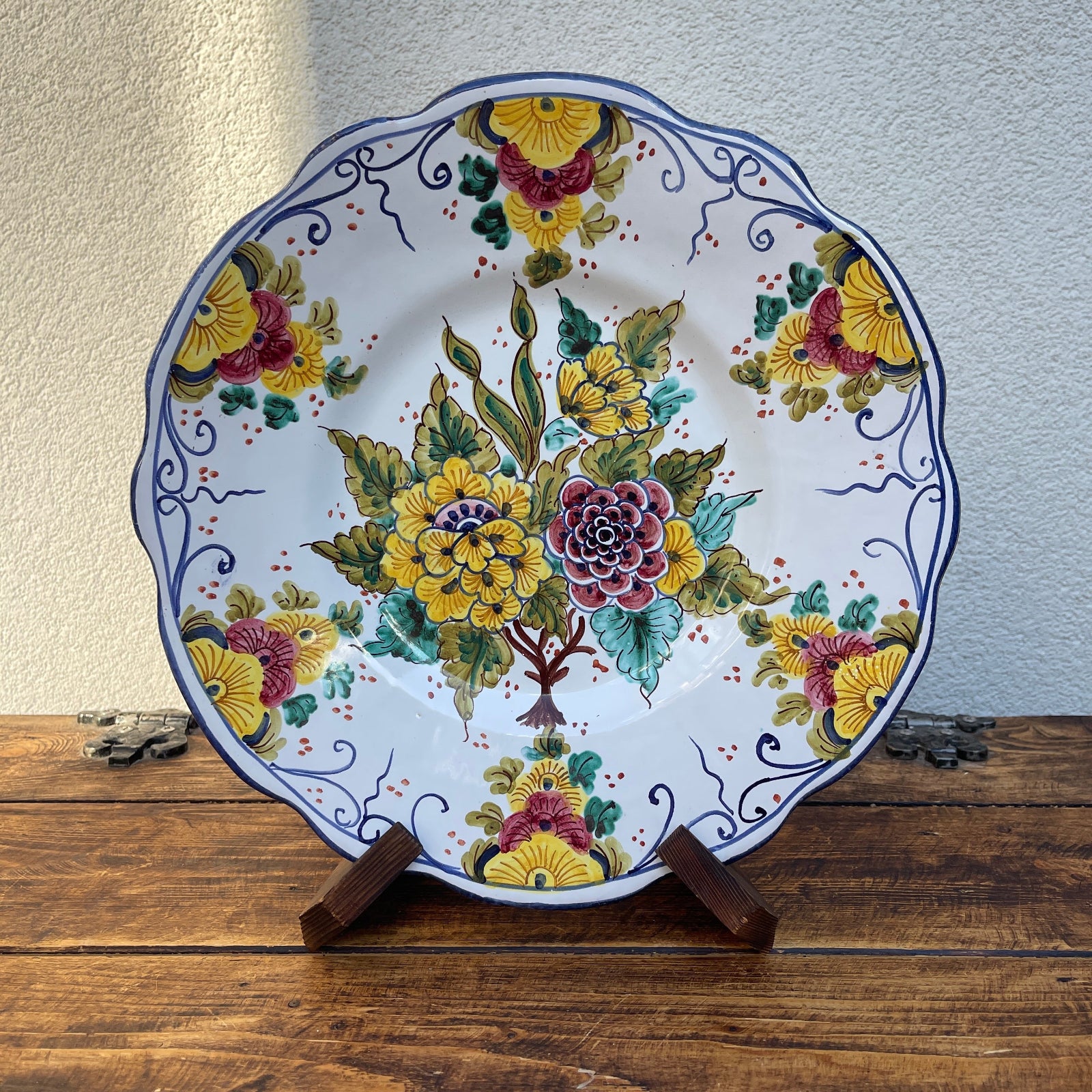 Decorative ceramic plate with floral design on a wooden stand against a neutral wall.