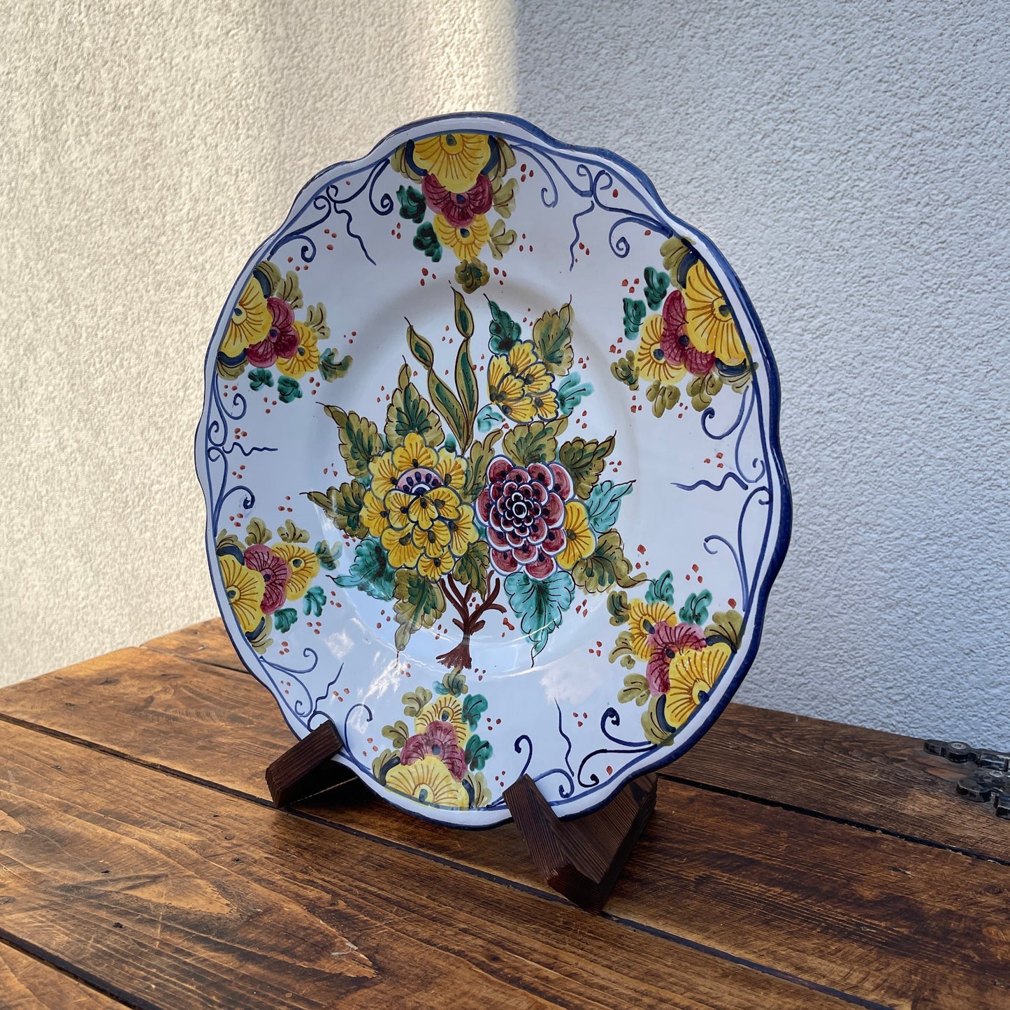 Decorative plate with floral design on a wooden stand against a neutral wall.