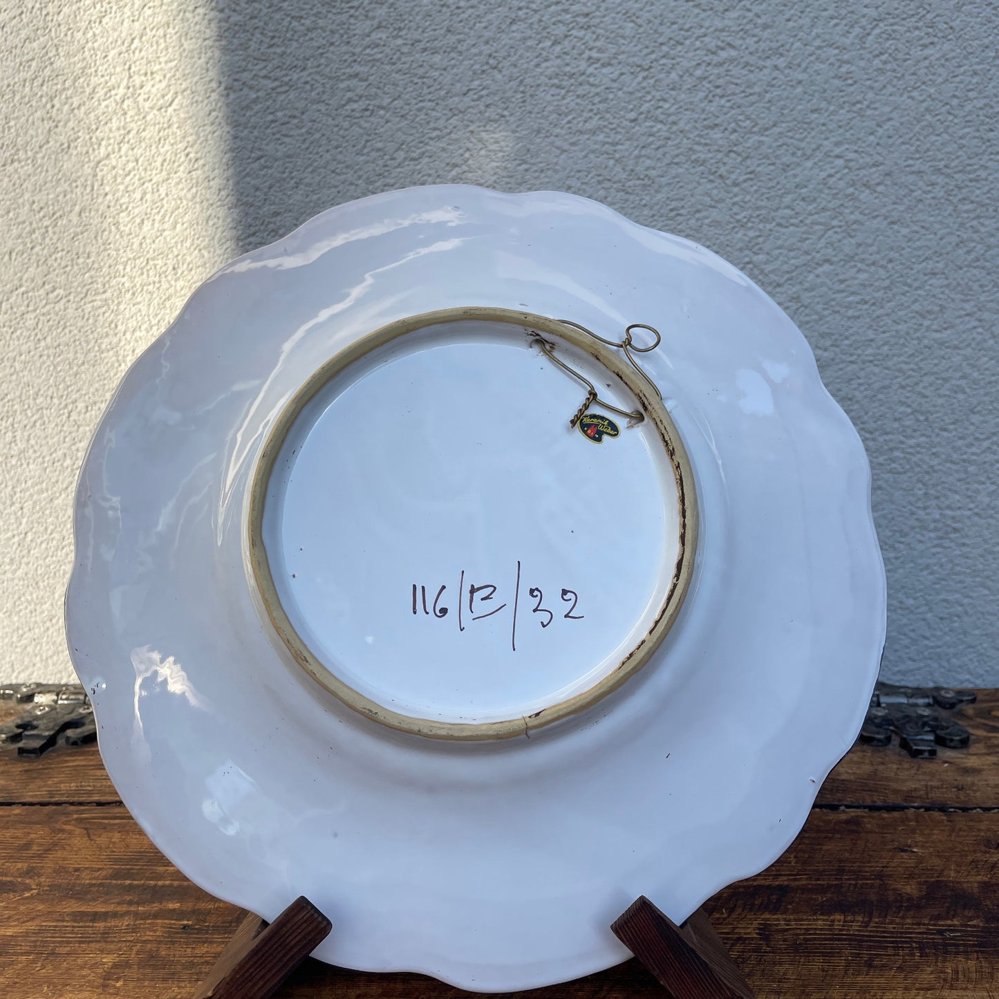 White ceramic plate with scalloped edge on a wooden stand against a light gray wall.