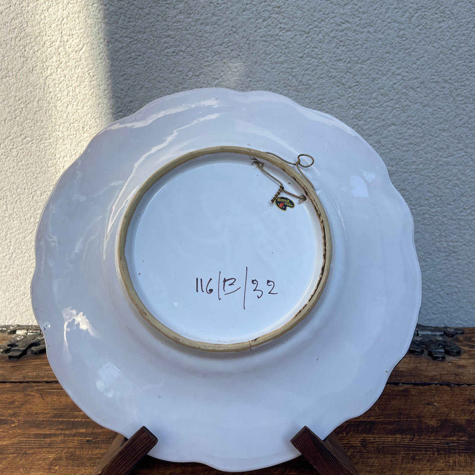 White ceramic plate with scalloped edge on a wooden stand against a light gray wall.