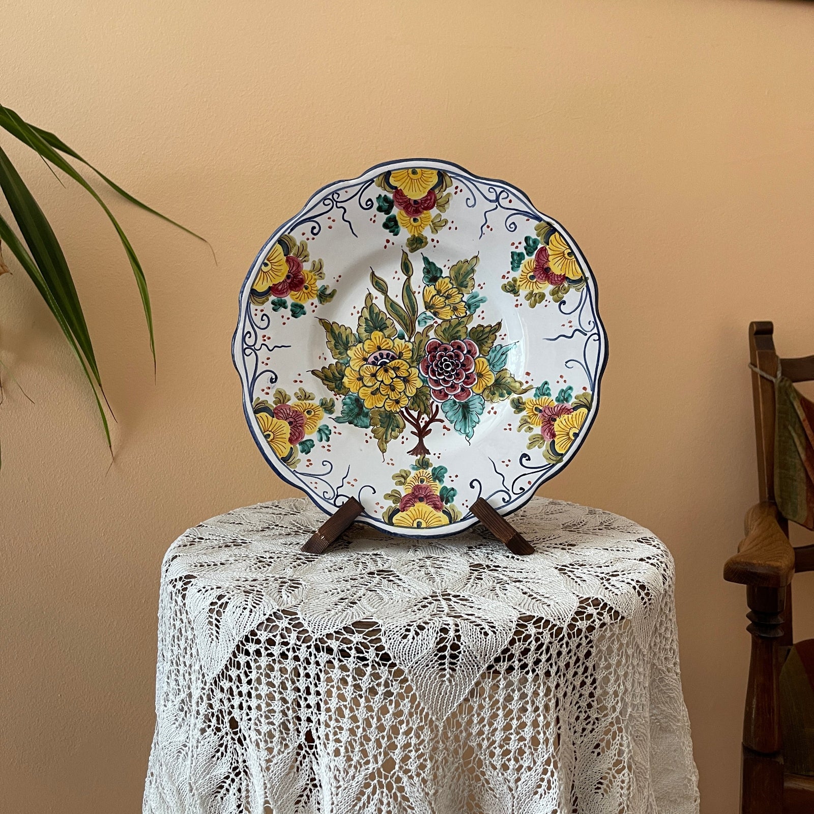 Decorative ceramic plate with floral design on a stand against a beige wall.