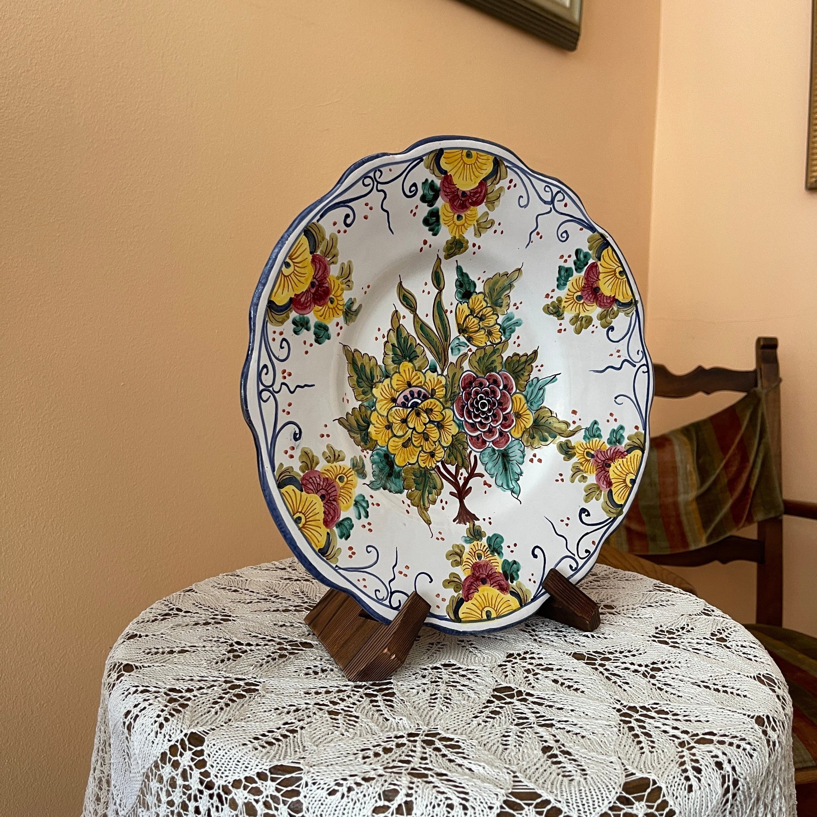 Decorative ceramic plate with floral design on a stand against a beige wall.