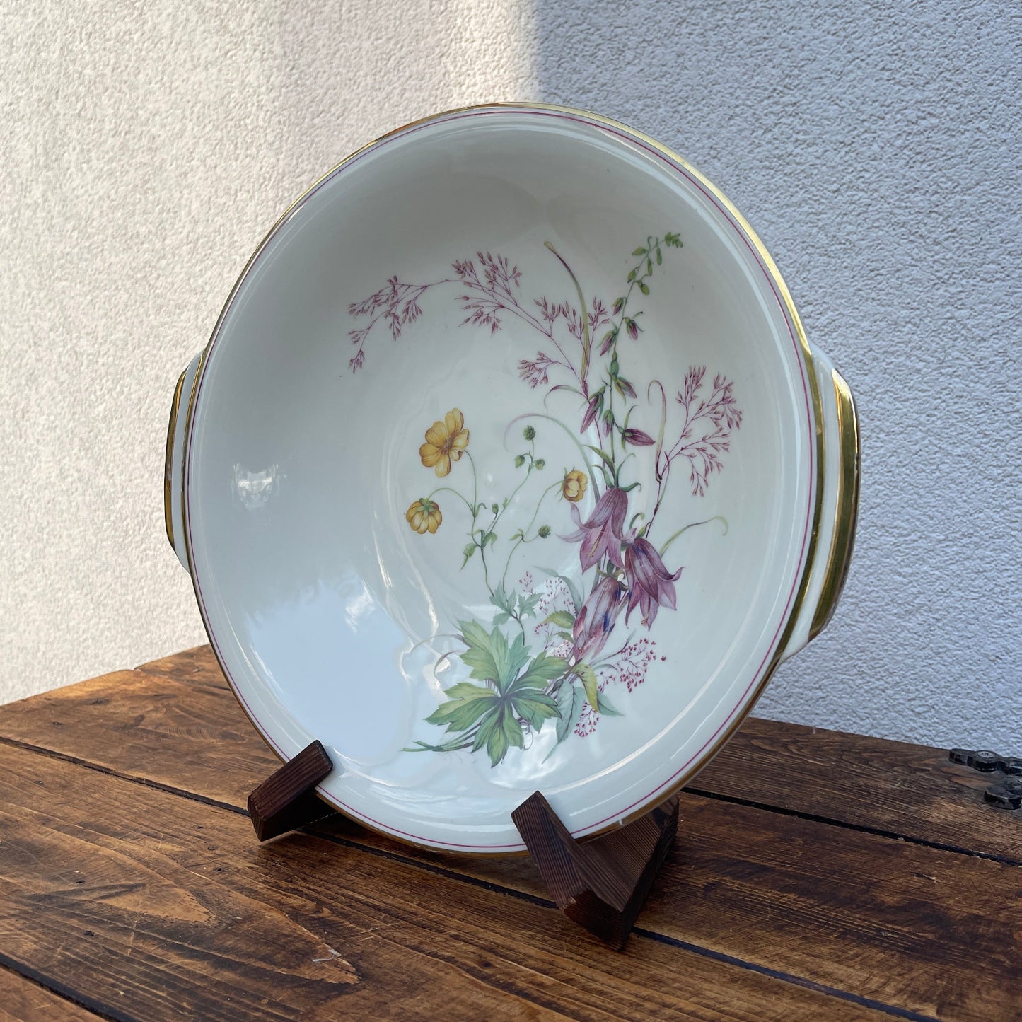 Decorative ceramic bowl with floral design on a wooden stand against a plain wall.