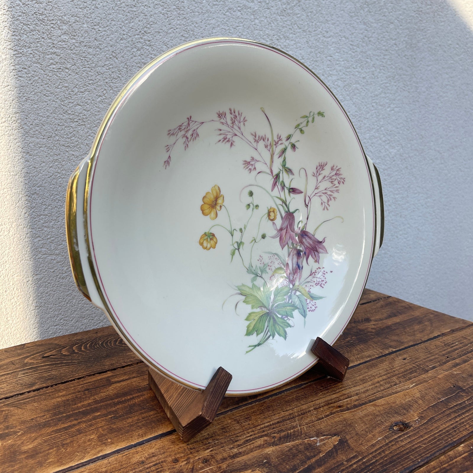 Decorative ceramic plate with floral design on a wooden stand against a gray wall.