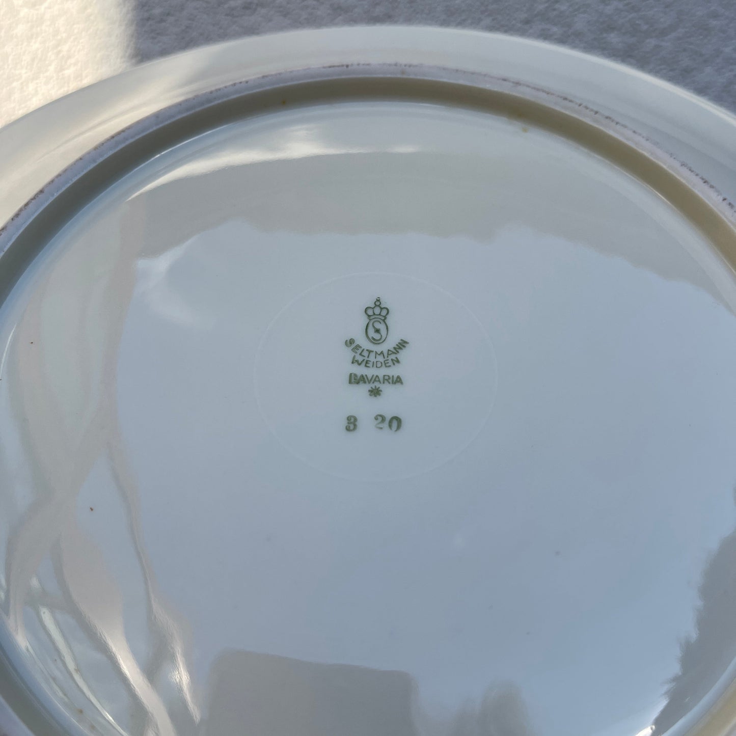 Close-up of a white ceramic plate with a visible brand logo and text on a light gray background.