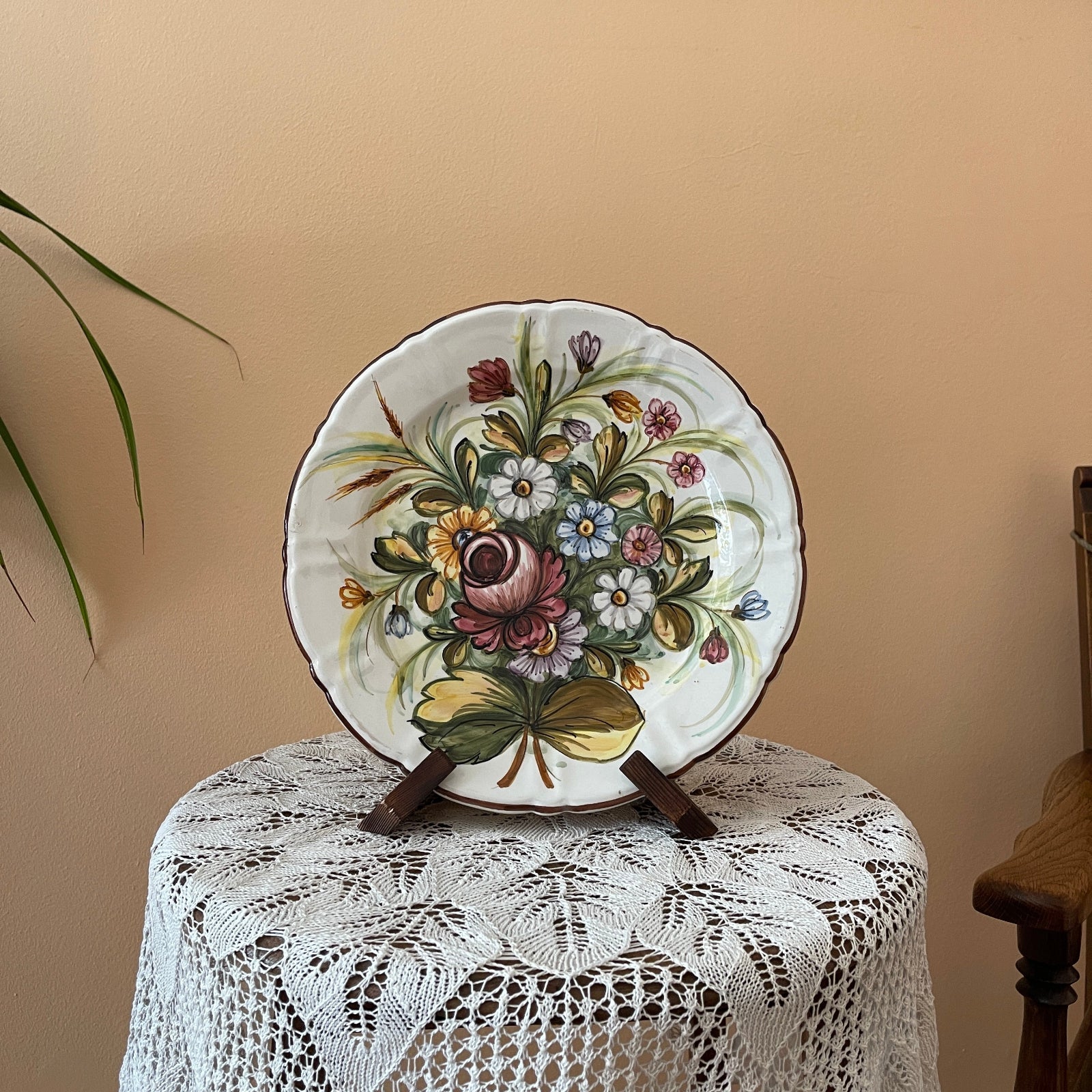 Decorative plate with floral design on a lace tablecloth against a beige wall.