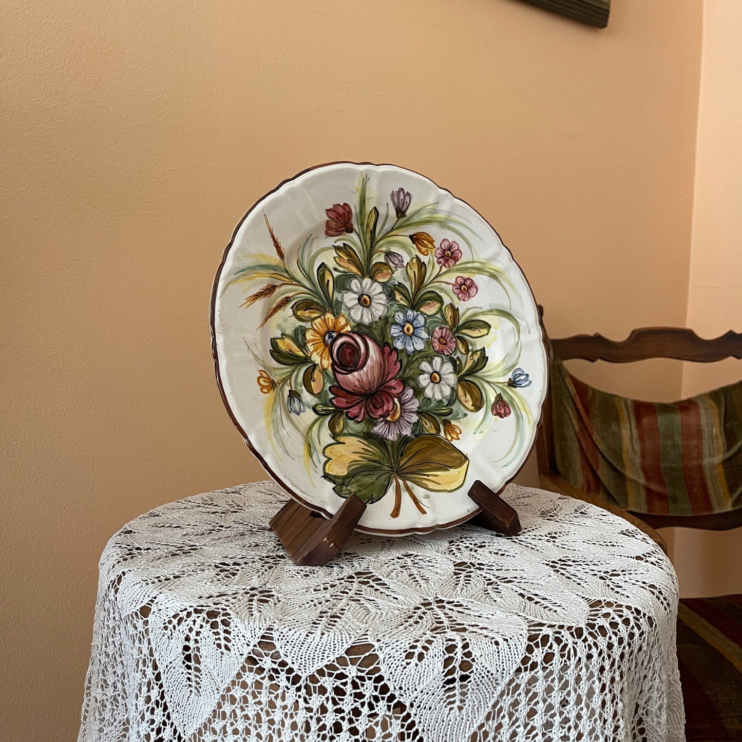 Decorative plate with floral design on a stand, placed on a lace tablecloth.