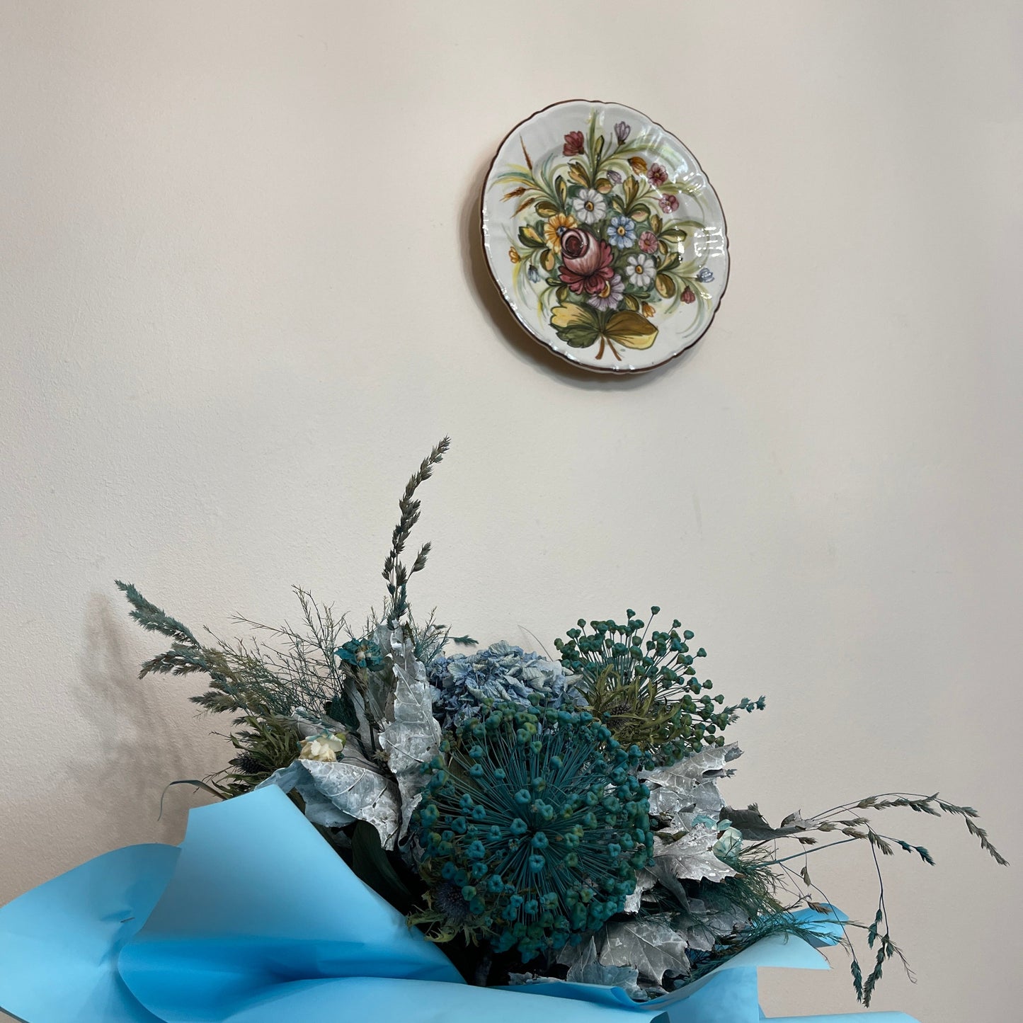 Decorative plate with floral design above a bouquet of flowers on a light background
