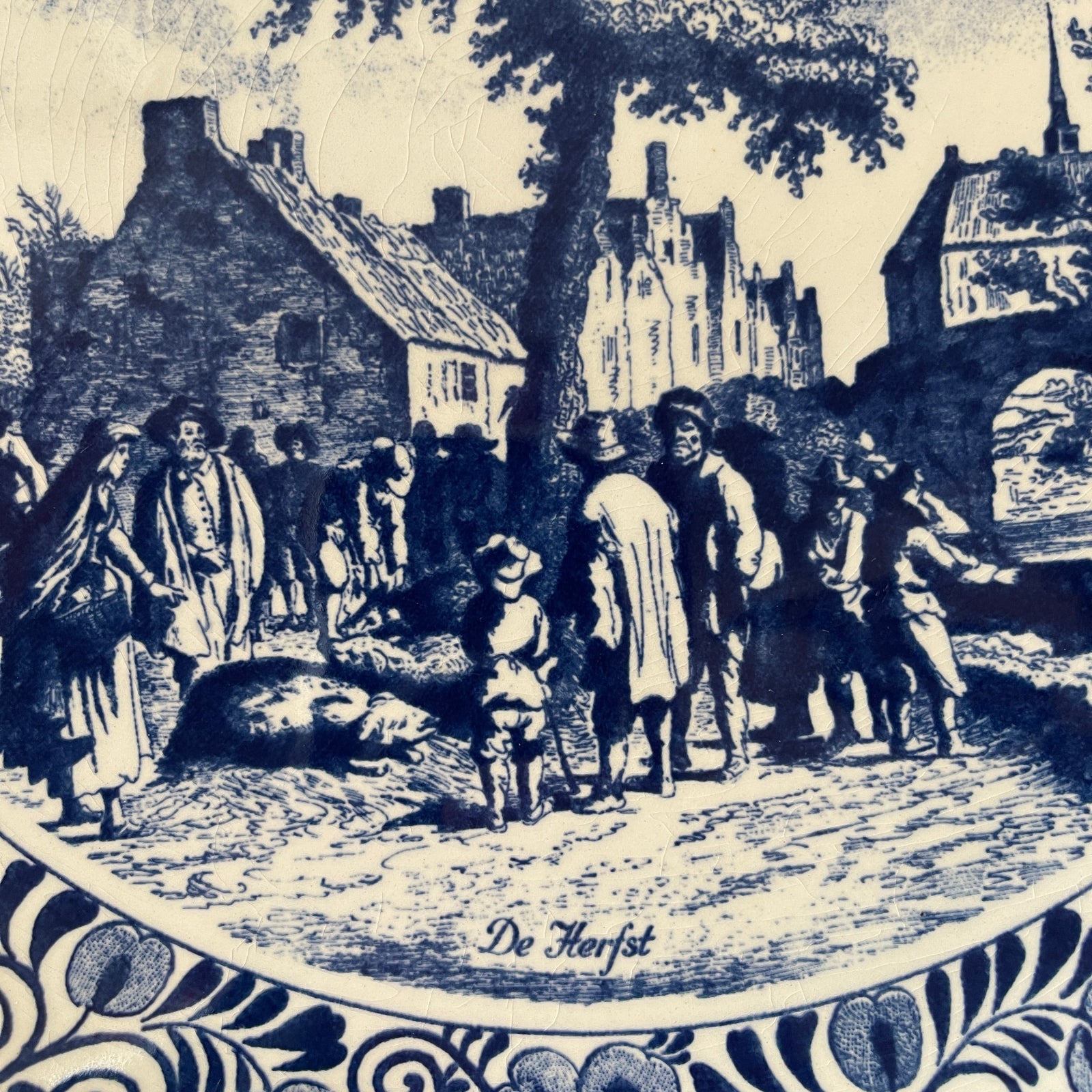 Vintage illustration of a village scene with people and animals, featuring the text 'De Herfst'.