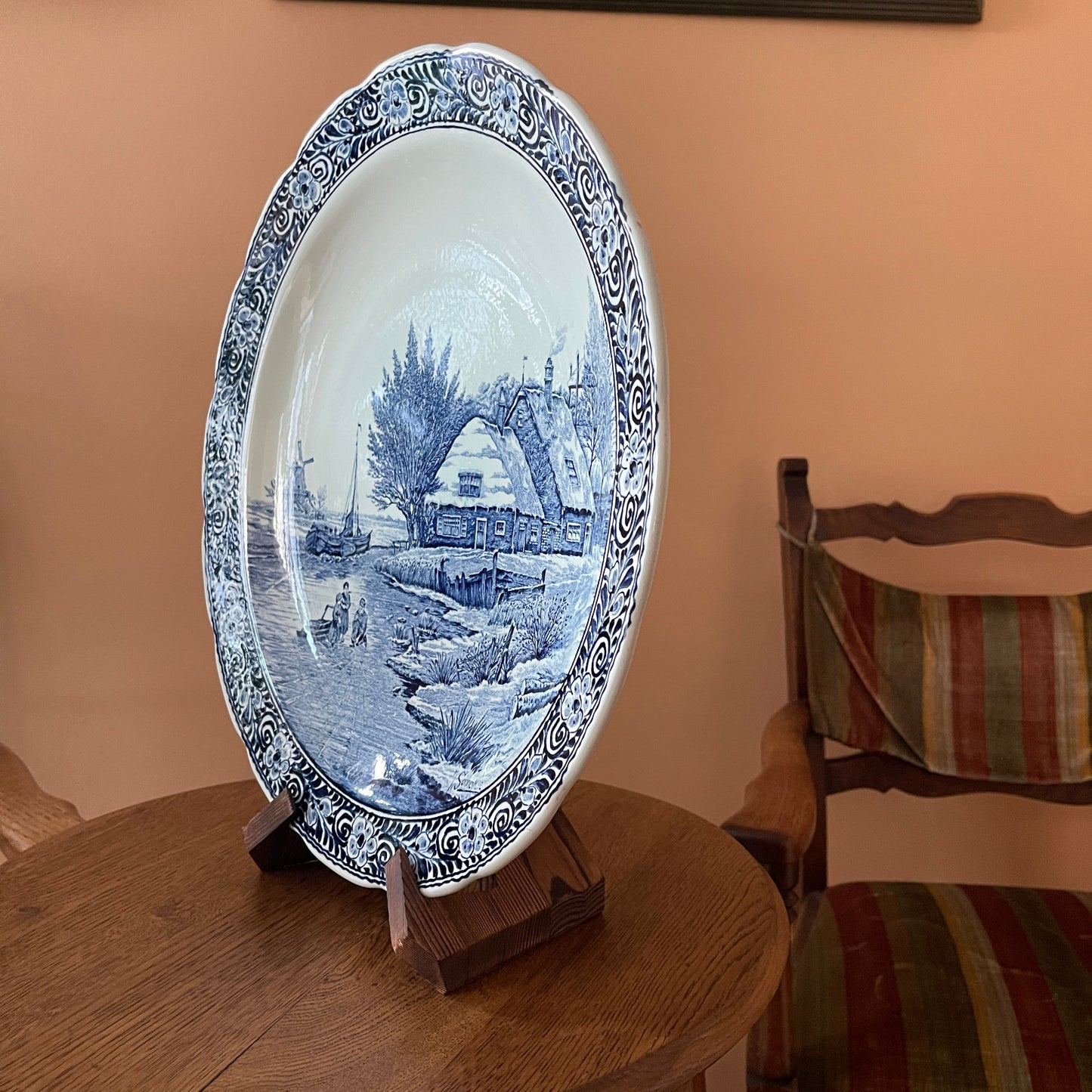 Decorative blue and white plate with a scenic design on a wooden stand against a beige wall.