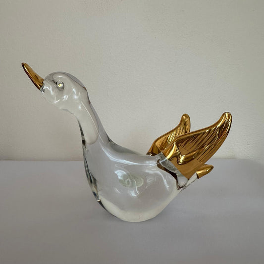 Glass duck figurine with gold wings on a plain background