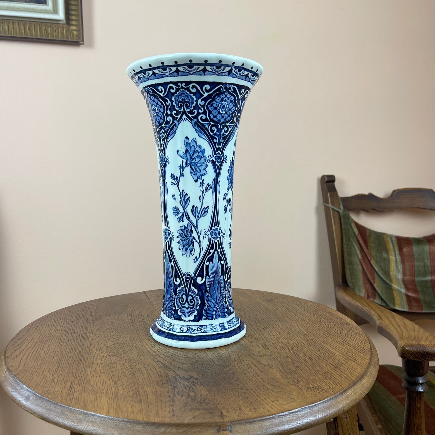 Blue and white ceramic vase on a wooden table with a chair and wall in the background