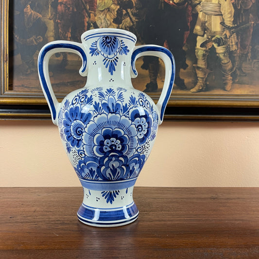 Blue and white floral-patterned vase on a wooden surface with a painting in the background