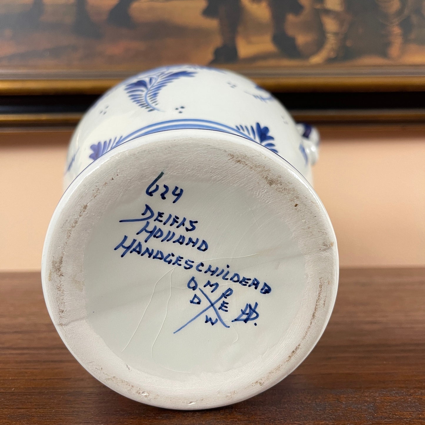 Back view of a white ceramic vase with blue floral patterns and visible branding on a wooden surface.