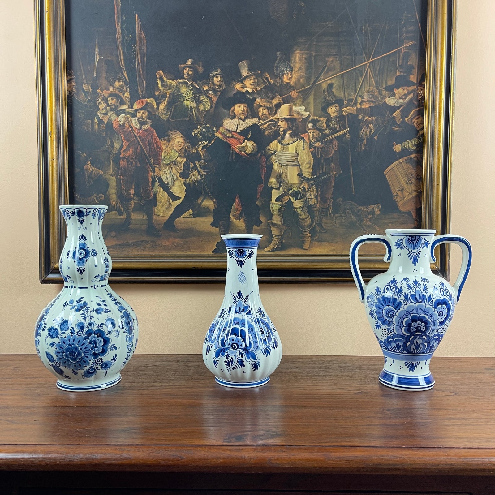 Three blue and white vases on a wooden surface with a large painting in the background.
