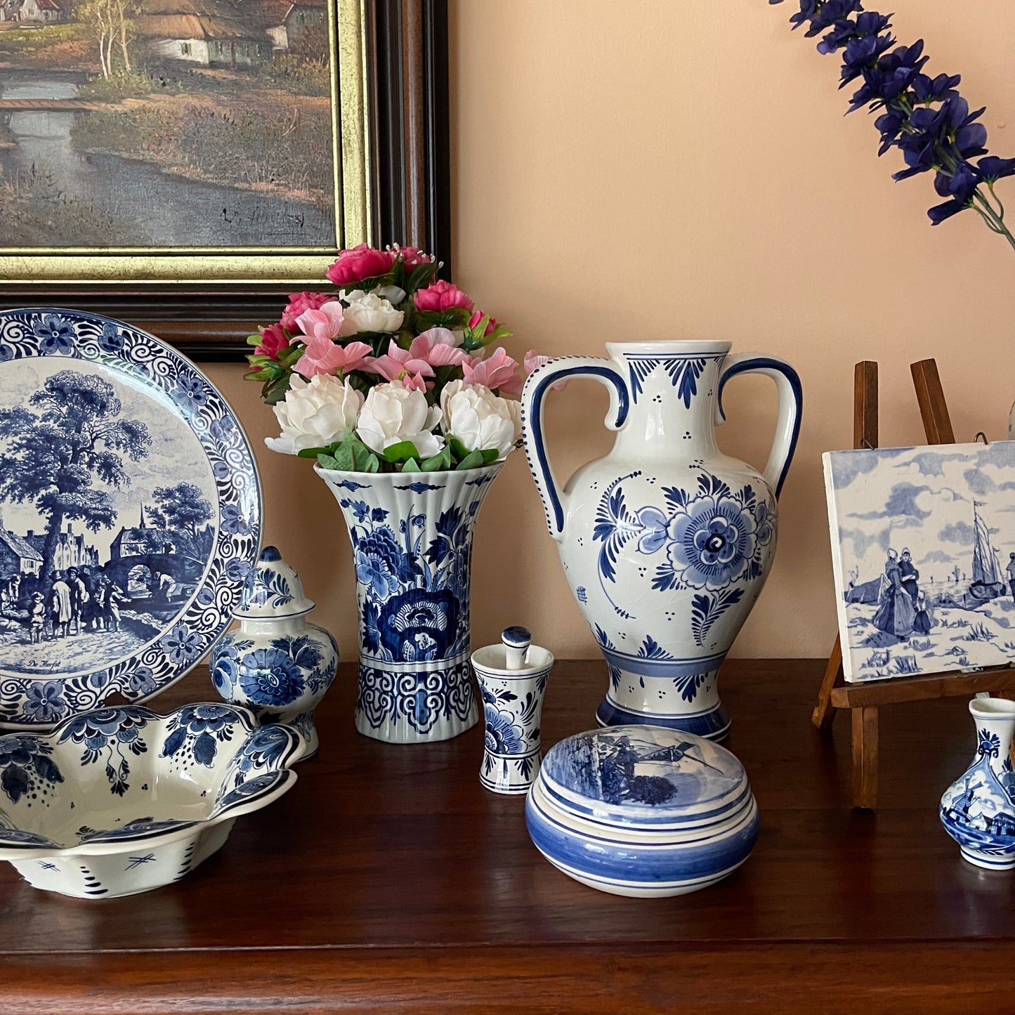 Collection of blue and white ceramic items on a wooden surface with a painting in the background.
