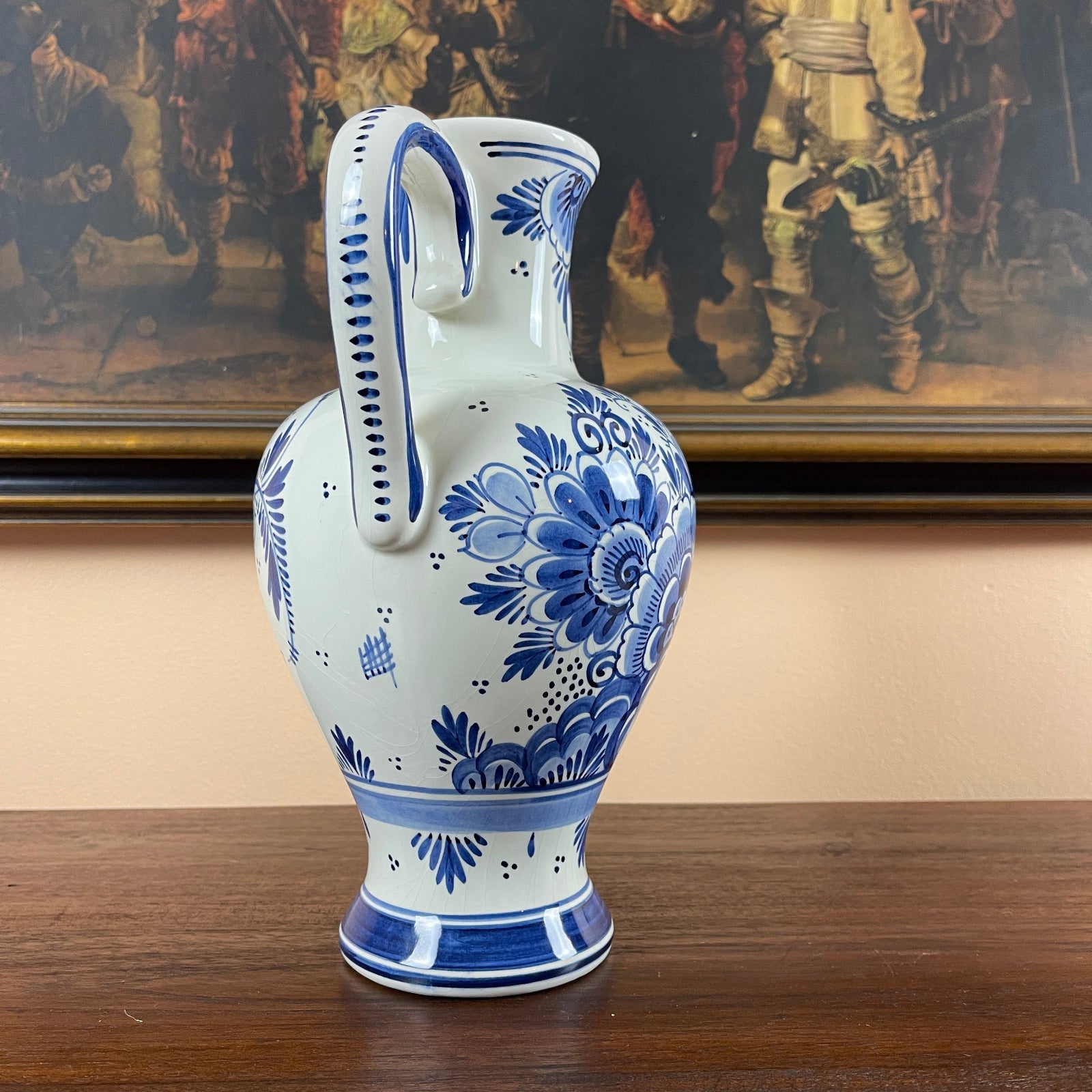 Blue and white ceramic vase on a wooden surface with a painting in the background